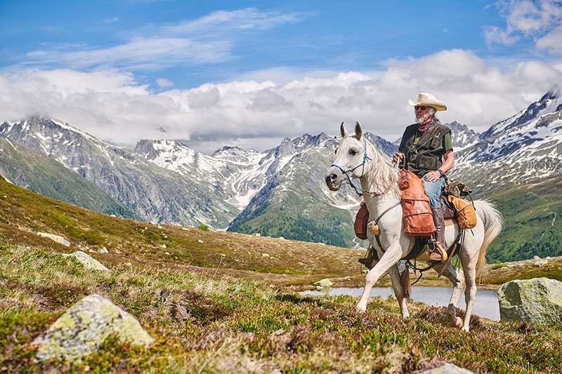 weisses Pferd mit Reiter in den Bergen