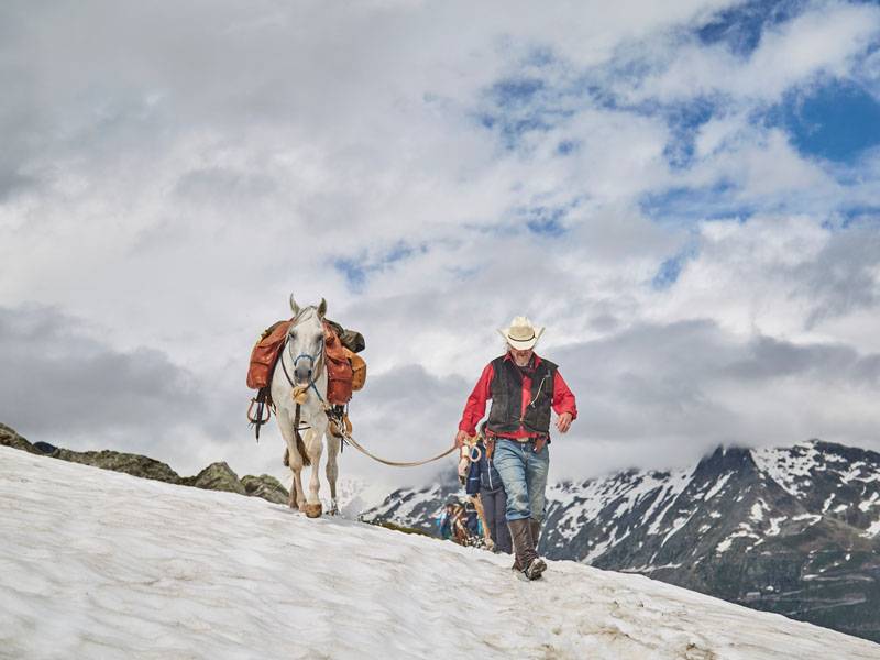 A trail rider leads his horse in the snow in the Alps