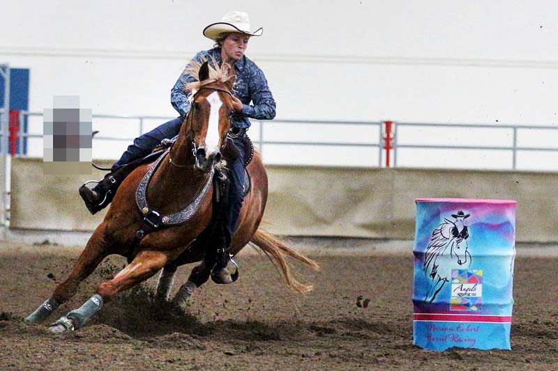 Une cavalière de barrel racing fait le tour d'un tonneau bleu